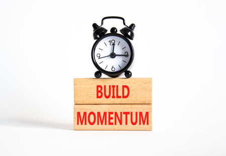 Build momentum symbol. Wooden blocks with words Build momentum. Beautiful white background with alarm clock. Business and Build momentum concept. Copy space.の写真素材