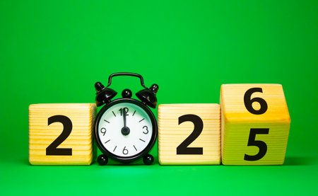 2026 New Year symbol. Businessman turns wooden cube and changes Year 2025 to 2026. Beautiful green background with Alarm clock. Copy space. Business and 2026 happy new year conceptの写真素材