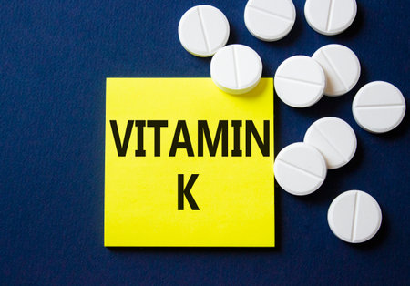 Vitamin K symbol. Concept word Vitamin K on yellow note. Beautiful deep blue background with pills. Medicine and Vitamin K concept. Copy spaceの写真素材
