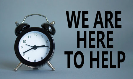 We are here to help symbol. Concept words we are here to help on wooden blocks. Beautiful gray background with alarm clock. Business and we are here to help concept. Copy space.の写真素材