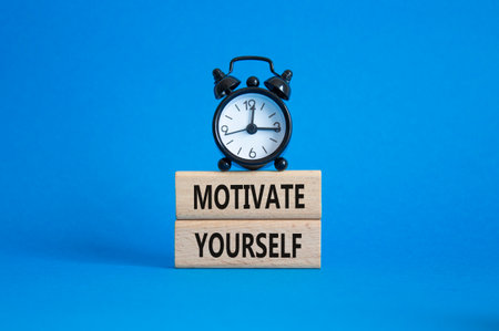 Motivation symbol. Concept words 'Motivate yourself' on wooden blocks. Beautiful blue background with alarm clock. Business and Motivate yourself concept. Copy space.の写真素材