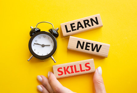 Learn new skills symbol. Concept words Learn new skills on wooden blocks. Businessman hand. Beautiful yellow background with alarm clock. Business and Learn new skills concept. Copy space.の写真素材