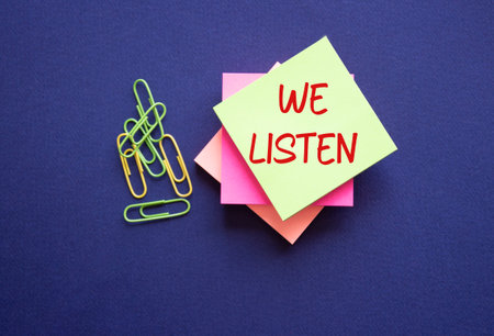 We listen symbol. Yellow sticky note with words We listen. Beautiful deep blue background. Business and We listen concept. Copy space.の写真素材