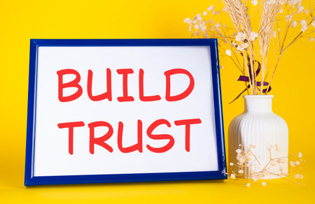 Build trust symbol. Concept words Build trust on beautiful wooden picture frame. Beautiful yellow background with flower vase. Business and Build trust concept. Copy space.の写真素材