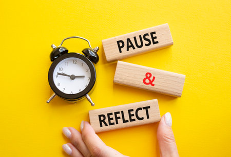 Pause and Reflect symbol. Concept words Pause and Reflect on wooden blocks. Businessman hand. Beautiful yellow background with alarm clock. Business and Pause and Reflect concept. Copy space.の写真素材