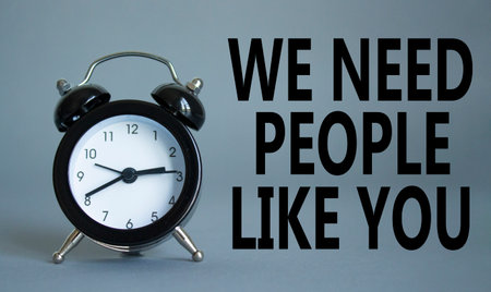 Hiring symbol. Wooden blocks with words We need People like You. Beautiful gray background with alarm clock. Business and Hiring concept. Copy space.の写真素材