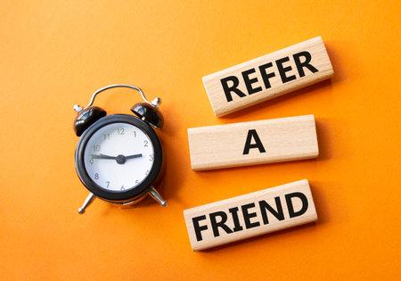 Refer a Friend symbol. Concept words Refer a Friend on wooden blocks. Beautiful orange background with alarm clock. Business and Refer a Friend concept. Copy space.の写真素材