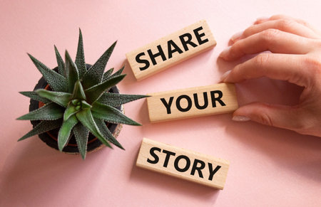 Share your story symbol. Wooden blocks with words Share your story. Beautiful pink background with succulent plant. Businessman hand. Business and Share your story concept. Copy space.の写真素材