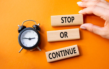 Stop or Continue symbol. Concept words Stop or Continue on wooden blocks. Businessman hand. Beautiful orange background with alarm clock. Business concept and Stop or Continue. Copy space.の写真素材