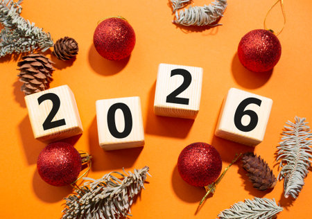 2026 New Year symbol. Wooden cubes with words 2026. Beautiful orange background with Christmas balls...
