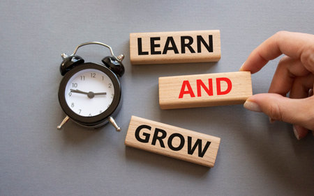 Learn and grow symbol. Concept words Learn and grow on wooden blocks. Businessman hand. Beautiful gray background with alarm clock. Business and Learn and grow concept. Copy space.の写真素材