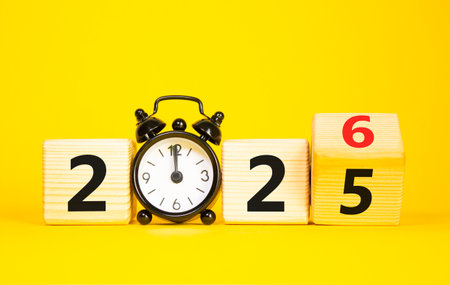 2026 New Year symbol. Businessman turns wooden cube and changes Year 2025 to 2026. Beautiful yellow background with Alarm clock. Copy space. Business and 2026 happy new year conceptの写真素材