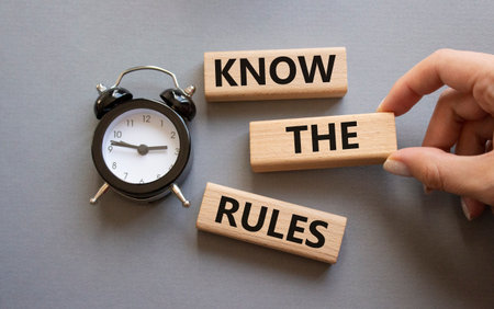 Know the rules symbol. Wooden blocks with words Know the rules. Businessman hand. Beautiful gray background with alarm clock. Business and Know the rules concept. Copy space.の写真素材