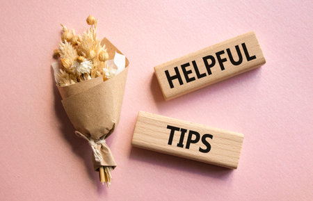 Helpful tips symbol. Wooden blocks with words Helpful tips. Beautiful pink background with bouquet of flowers. Business and Helpful tips concept. Copy space.の写真素材