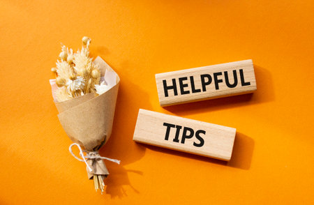 Helpful tips symbol. Wooden blocks with words Helpful tips. Beautiful orange background with bouquet of flowers. Business and Helpful tips concept. Copy space.の写真素材