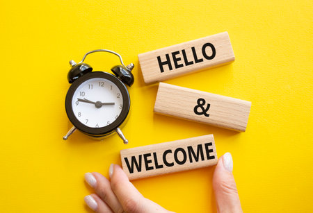 Hello and Welcome symbol. Concept words Hello and Welcome on wooden blocks. Businessman hand. Beautiful yellow background with alarm clock. Business and Hello and Welcome concept. Copy space.の写真素材