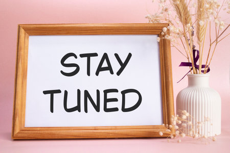 Stay Tuned symbol. Concept words Stay Tuned on beautiful wooden picture frame. Beautiful pink background with flower vase. Business and Stay Tuned concept. Copy space.の写真素材