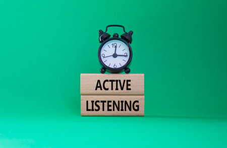 Listen actively symbol. Wooden blocks with words Listen actively. Beautiful green background with alarm clock. Business and Active listening concept. Copy space.の写真素材