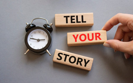 Tell your story symbol. Wooden blocks with words Tell your story. Businessman hand. Beautiful gray background with alarm clock. Business and Tell your story concept. Copy space.の写真素材