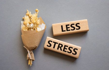 Less stress symbol. Wooden blocks with words Less stress. Beautiful gray background with bouquet of flowers. Healthcare and Less stress concept. Copy space.の写真素材