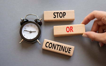 Stop or Continue symbol. Concept words Stop or Continue on wooden blocks. Businessman hand. Beautiful gray background with alarm clock. Business concept and Stop or Continue. Copy space.の写真素材