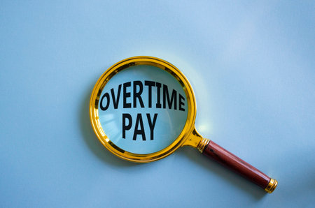 Overtime Pay symbol. Magnifying Glass with words Overtime Pay. Beautiful blue background. Business and Overtime Pay concept. Copy space.の写真素材
