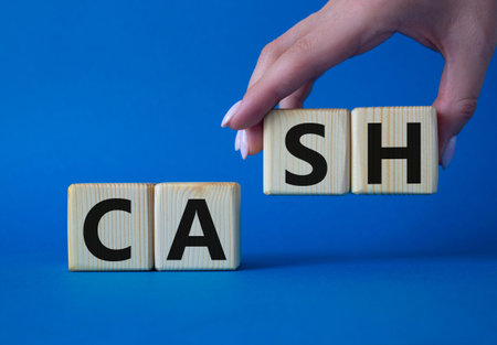 Cash symbol. Concept Cash word on wooden cubes. Beautiful blue background. Businessman hand. Business and Cash concept. Copy space.の写真素材