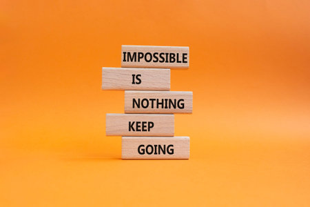 Keep Going symbol. Wooden blocks with words Impossible is Nothing Keep Going. Beautiful orange background. Business and Keep Going concept. Copy spaceの写真素材
