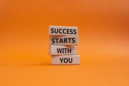 Success symbol. Wooden blocks with words Success Starts With You. Beautiful orange background....