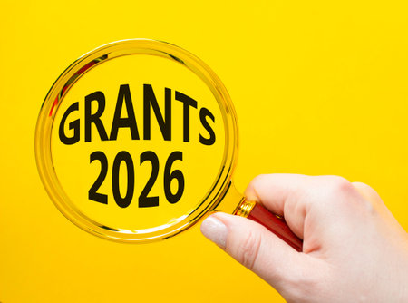 Grants 2026 symbol. Magnifying Glass with words Grants 2026. Businessman hand. Beautiful yellow...
