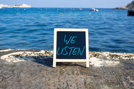 We listen symbol. Concept words We listen on black chalk background. Beautiful sea background. Business and We listen concept. Copy space.