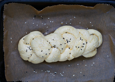 Homemade challah prepared for baking, white wicker bread sprinkled with white and black sesame seeds...