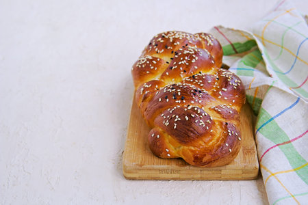 Homemade sliced challah, traditional wicker white bread on a wooden board on a light concrete...