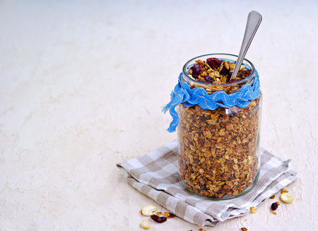 Homemade baked oat granola with nuts, dried cranberries and honey in a glass jar on a light concrete background. Granola recipes. Healthy breakfast.の写真素材