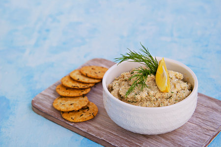 Appetizer, fish pate from mackerel, boiled eggs and onions in a white ceramic bowl on a blue concrete background. Served with savory crackers. Fish recipes.の写真素材