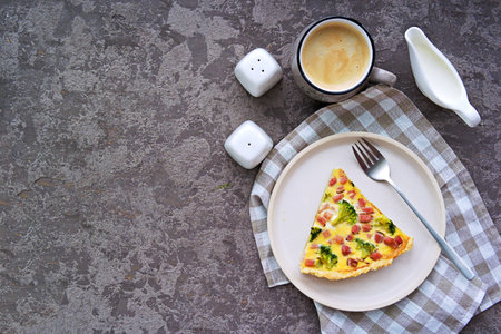 Open savory shortcrust pastry pie with ham, broccoli and egg filling on a gray concrete background....