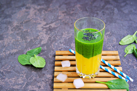 A healthy drink, a two-layer smoothie with fresh spinach and ripe mango in a tall glass glass on a dark concrete background. Drinks for detox and weight loss. Copyspaceの写真素材