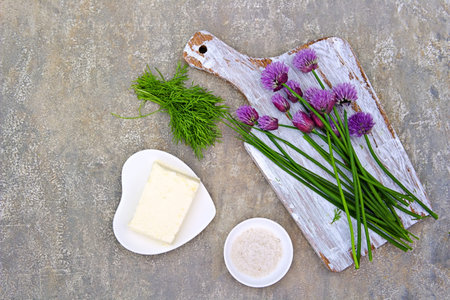 Prepared Ingredients for butter with garlic, herbs and flowers chives on a gray concrete background.