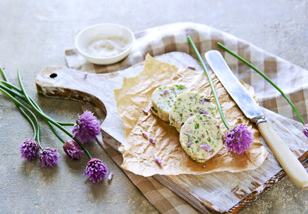 Sliced washers herbs butter with garlic, dill and chives flowers on a wooden board on a gray concrete background. Herbal Butter Recipes.の写真素材