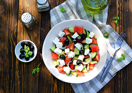 Vegetable salad with feta cheese and olives in a light ceramic bowl on a wooden background. Salad recipes. Mediterranean food.の写真素材