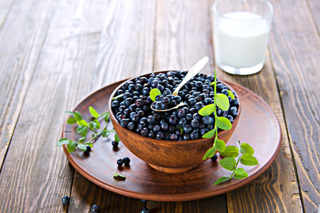Fresh wild blueberries in a clay brown bowl and a glass of milk on a wooden background. Healthy food, snacks. Selective focusの写真素材