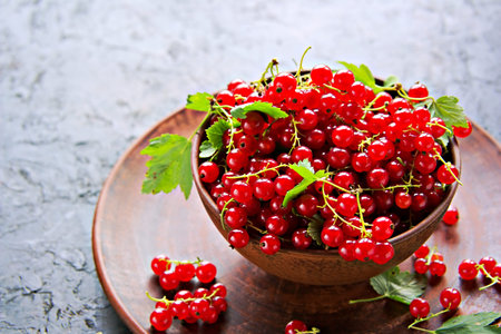 Fresh juicy berries of red currant in a clay bowl on a black concrete background. Harvest red...