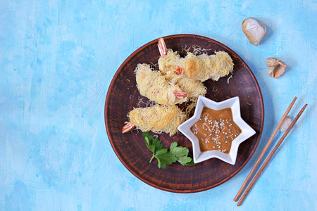 Snack or lunch, large shrimp in a crispy dough Kataify on a clay plate. Served with peanut sauce. Asian cuisine. Top view, copy space.の写真素材