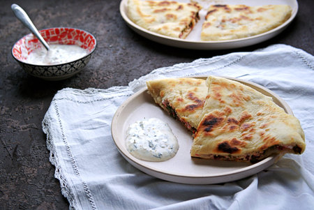 Ossetian pie with beet tops and cheese on a white clay plate. Served with sour cream, garlic and...