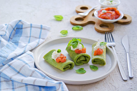 Spinach pancakes rolled up on a white plate on a light concrete background. Served with salted salmon and soft cheese. Spinach recipes. Copyspace.の写真素材