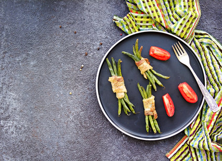 Hot appetizer, a bundle of green beans wrapped in bacon on a black plate on a dark concrete background. Snack recipes. Thanksgiving Day.の写真素材