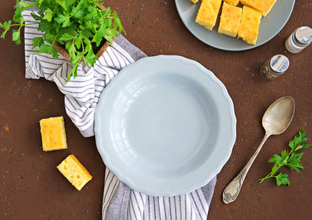 Table setting: two gray plates, striped towel, salt shaker, pepper shaker and spoon on a brown...