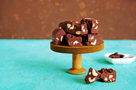 Sliced homemade fudge chocolates made from dark chocolate, condensed milk and hazelnuts on a wooden stand on a turquoise concrete background. Candy recipes. American cuisine. Valentine's dayの写真素材