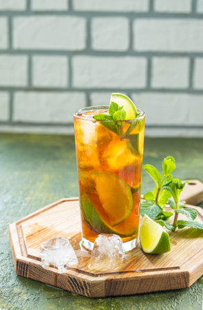 Refreshing drink, iced tea with lime wedges in glasses on a wooden board on a green concrete background. Summer drinks. Soft drinksの写真素材
