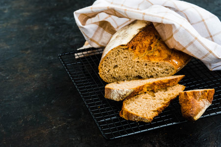 Sliced loaf of homemade wheat bread on a black wire rack against a dark concrete background. Bread...